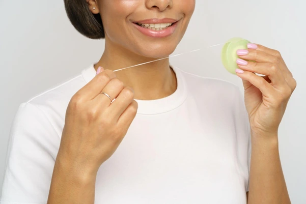 A smiling woman using dental floss to clean her teeth