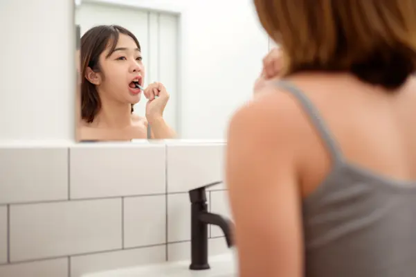 A woman brushing her teeth as part of a good oral hygiene routine to prevent bad breath