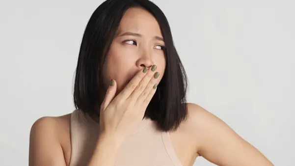 A young woman covering her mouth, concerned about having bad breath or halitosis
